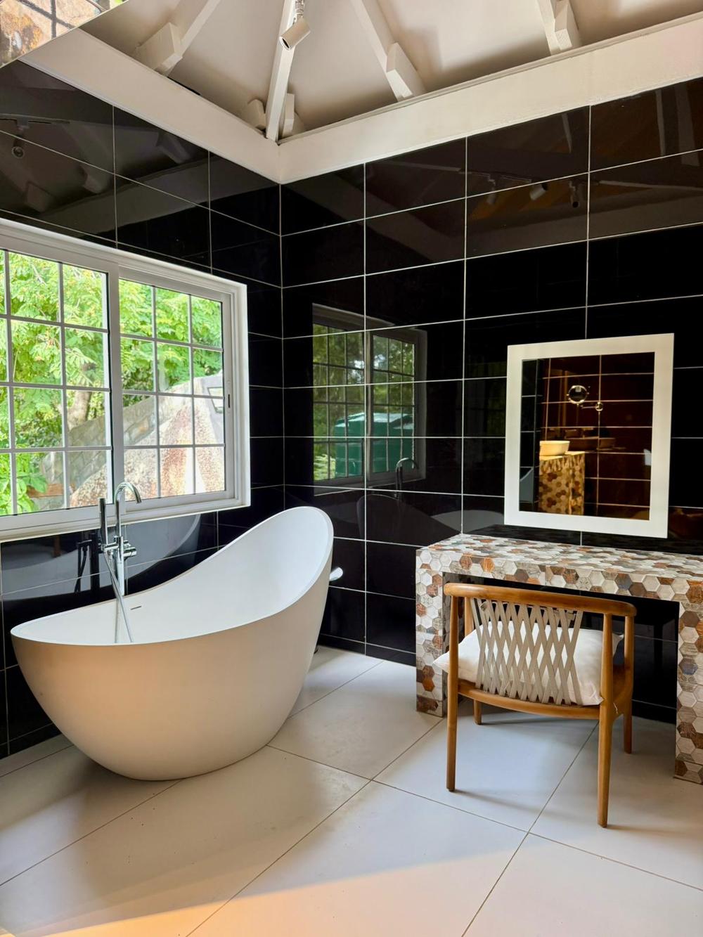 Master bathroom with freestanding white bath against black gloss tile and forest view