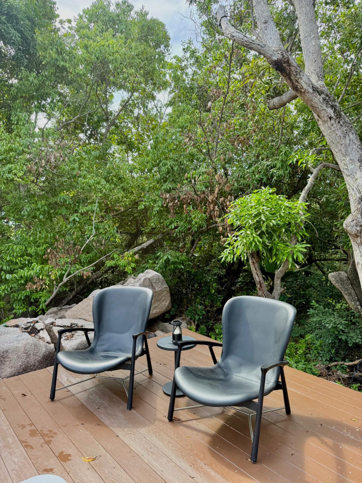 Two leather lounge chairs on the timber deck, in the shade of takamaka trees