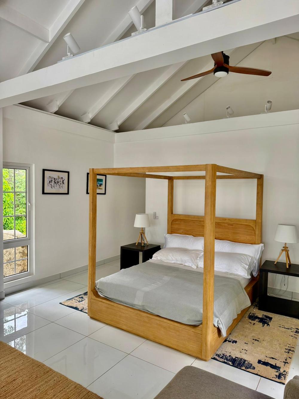 The master suite with carved teak four-poster bed under a vaulted white ceiling